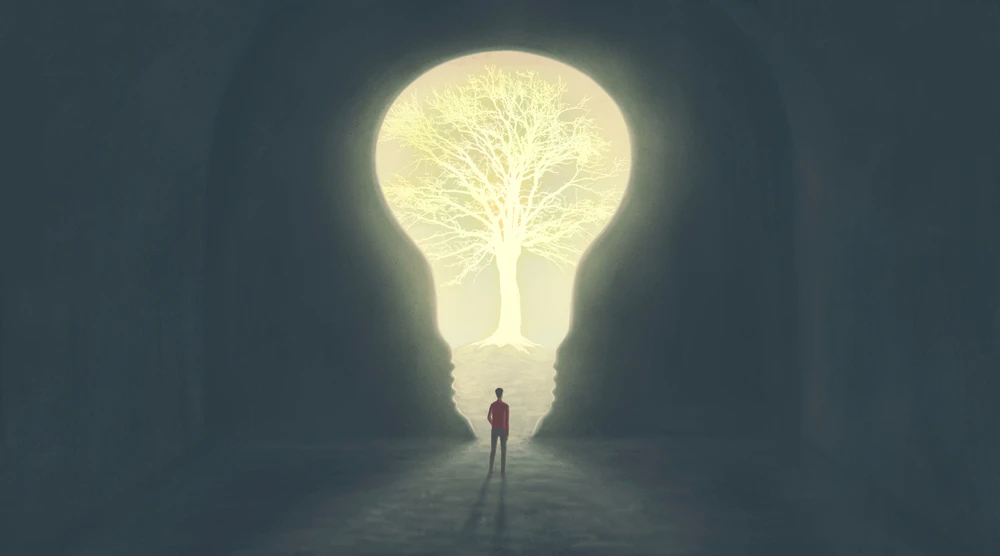 電球の形をした光の中に一本の木が浮かび、その前に人が立っているイメージ